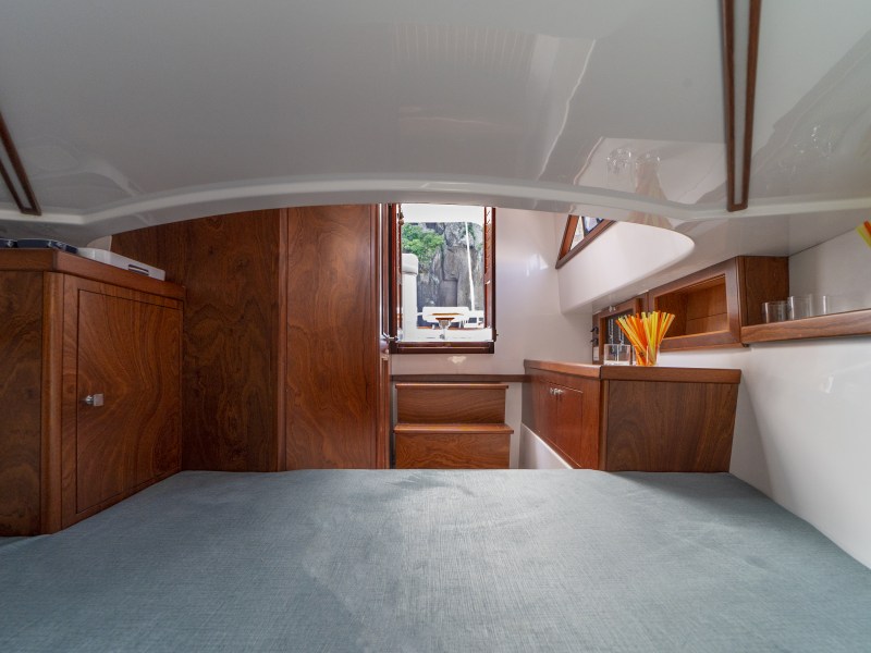 Boat cabin interior with wood cabinets and gray bed, open door view outside.