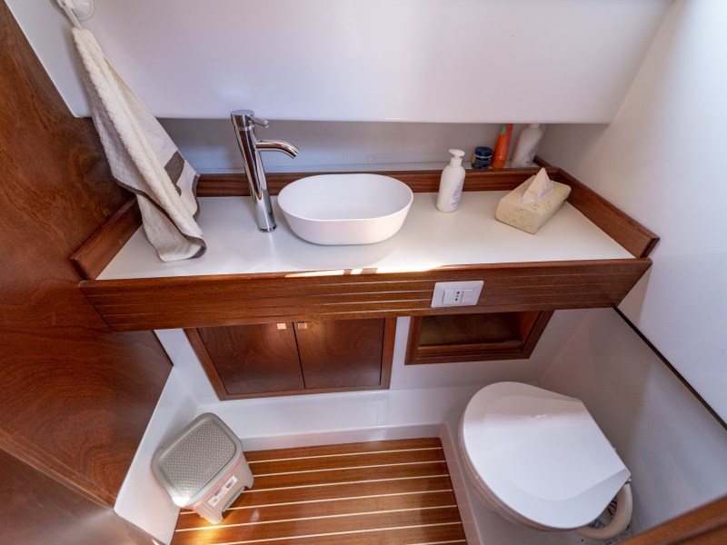Compact bathroom with wooden accents, featuring a sink, mirror, toilet, and a small waste bin.