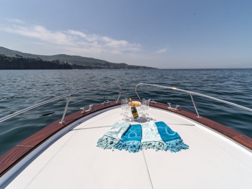 Boat deck with towels and a bottle on calm sea, coastline visible under clear sky.