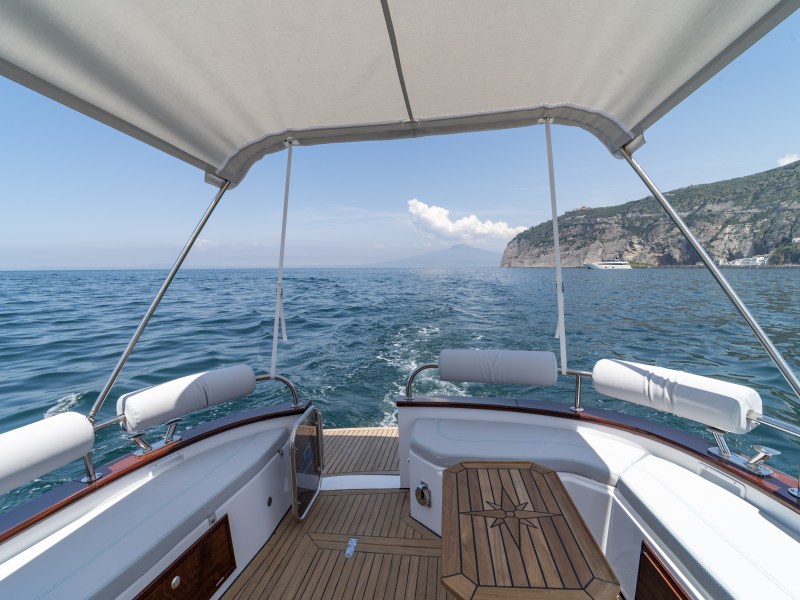 View from a boat's deck on open sea under a canopy, mountains in the distance.