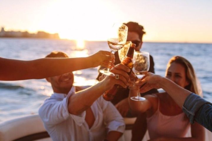 Group of friends toasting with drinks on a boat at sunset.