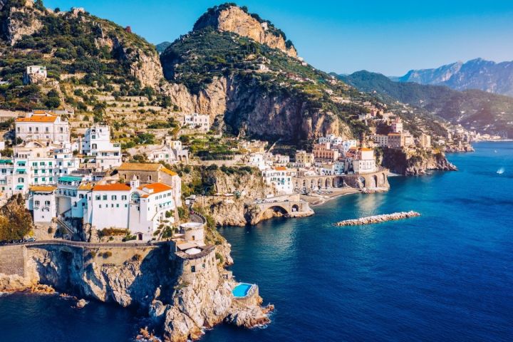 Coastal town with colorful buildings on cliffs, overlooking a blue sea with distant mountains.
