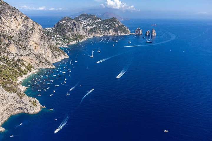 Aerial view of rocky coastline with boats on a clear blue sea under a sunny sky.