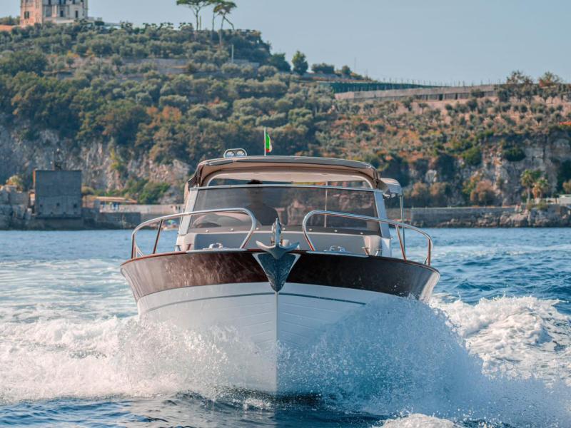 A boat navigating through clear water with a scenic hillside in the background.