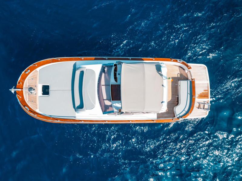 Aerial view of a yacht with brown trim floating on deep blue ocean water.