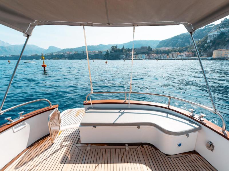 View of a town from a boat's deck on a sunny day with mountains in the background.
