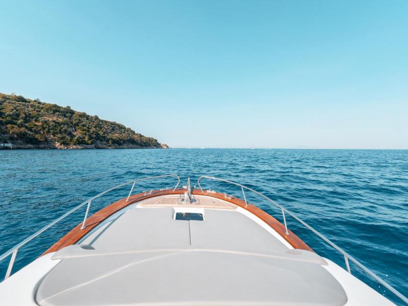 Bow of a boat facing calm blue sea with a distant green coastline under clear sky.