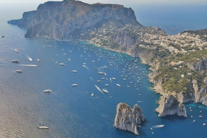 Aerial view of a coastal area with cliffs, numerous boats, and blue sea under a clear sky.