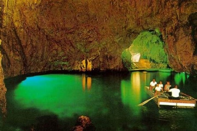 Boat with people inside a lit cave with green water.