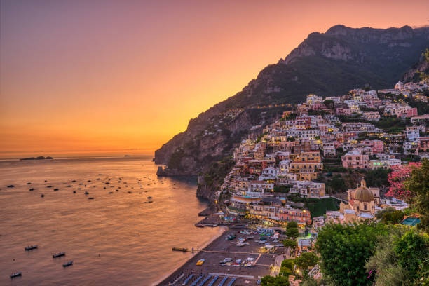 Colorful cliffside village at sunset by the sea, boats and calm water.