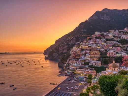 Colorful cliffside village at sunset by the sea, boats and calm water.
