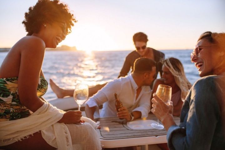 Group of friends laughing and toasting on a boat during sunset.