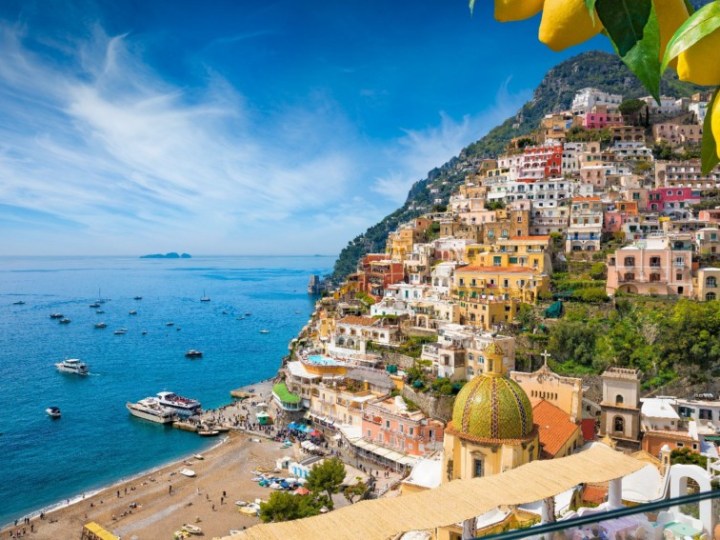 Colorful coastal town on a hill with boats in the sea and lemons hanging above.