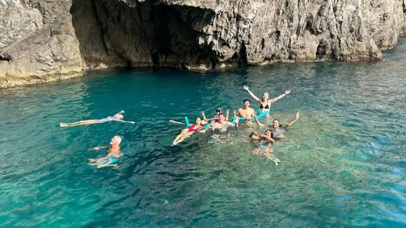 Group of people swimming near a rocky cliff in clear blue water.