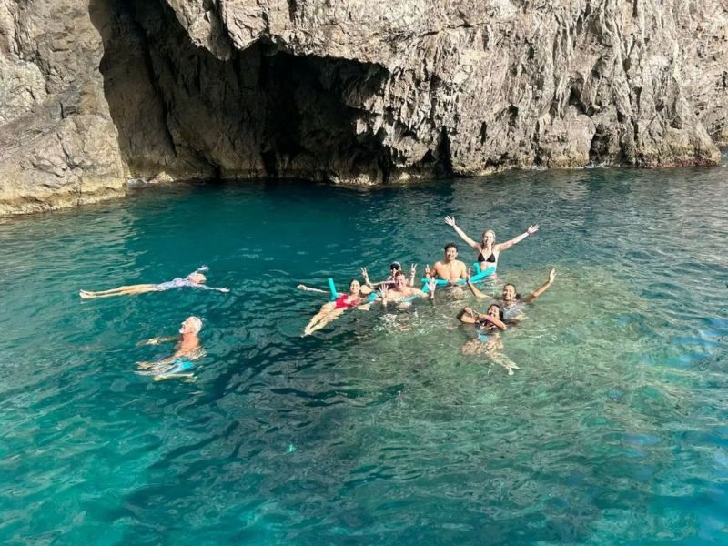 Group of people swimming near a rocky cliff in clear blue water.
