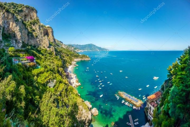 Scenic coastal view with cliffs, green vegetation, and boats on a blue sea.