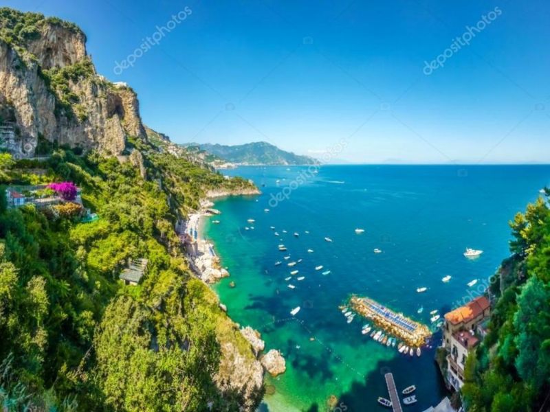 Scenic coastal view with cliffs, green vegetation, and boats on a blue sea.