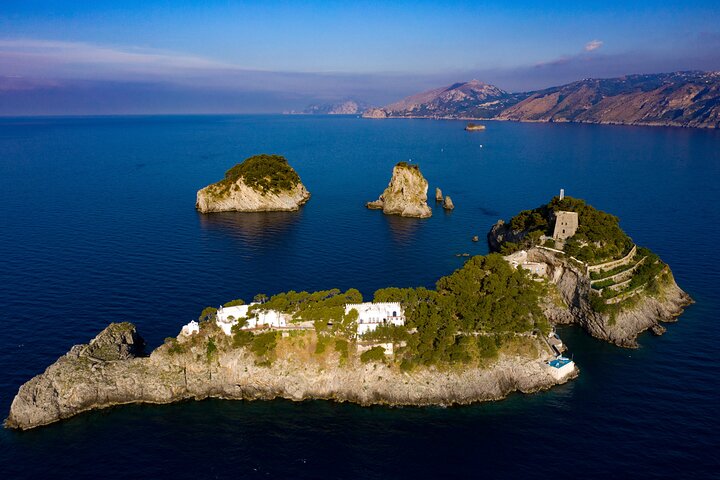 Aerial view of islands with green vegetation and a stone building, surrounded by blue sea.