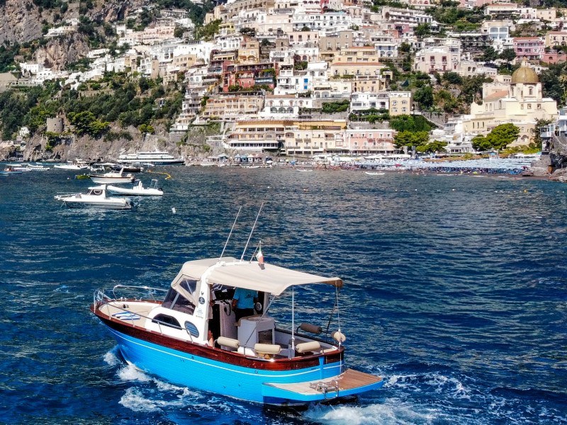 Boat on blue water with colorful hillside town in background.