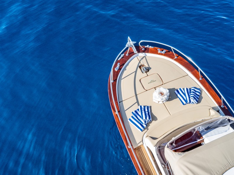 Aerial view of a boat with tan deck and blue-striped towels on clear blue water.