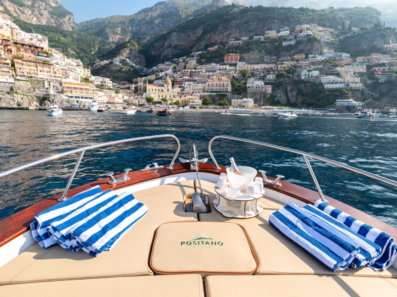 Boat deck with striped towels facing colorful coastal buildings and cliffs in Positano, Italy.