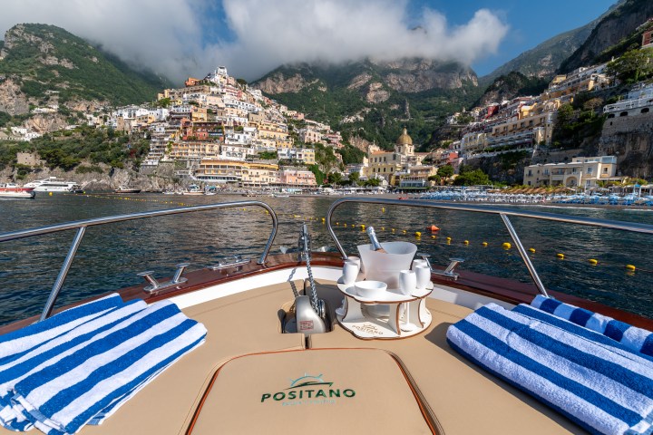 View from a boat with striped towels, looking at the colorful hillside of Positano under a cloudy sky.
