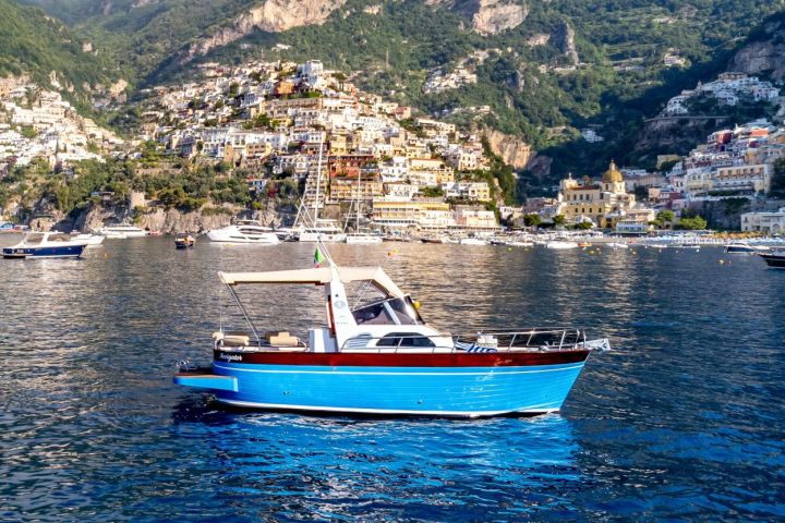 Blue boat on water with colorful hillside town in the background.