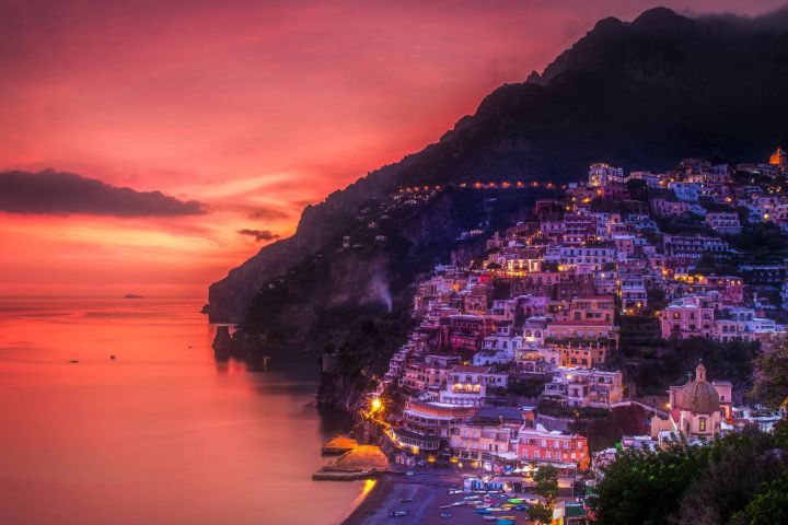 Coastal town at dusk with colorful buildings and a vibrant red sunset sky.
