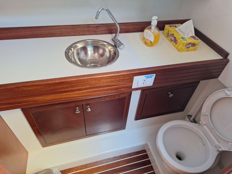 Small bathroom with a sink, soap dispenser, tissue box, and a toilet on a wooden floor.