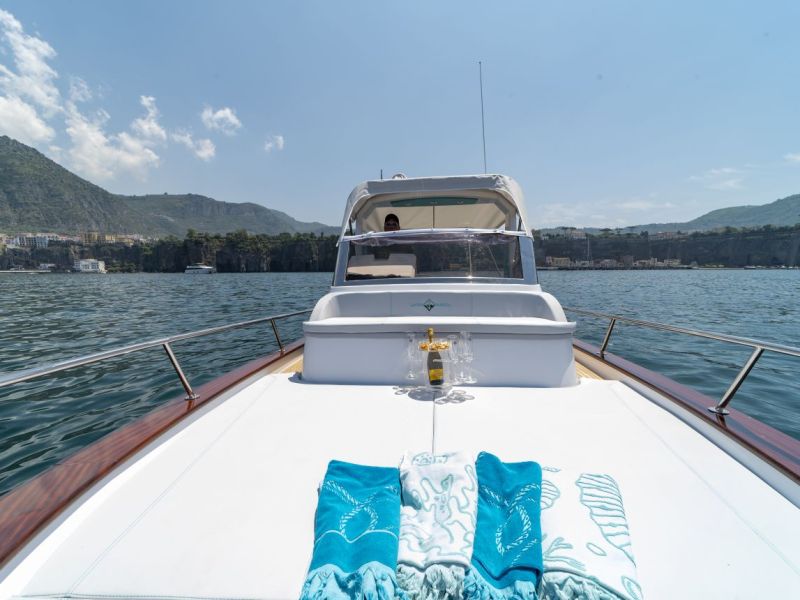 Boat deck with towels, champagne, glasses, and scenic coastal view.