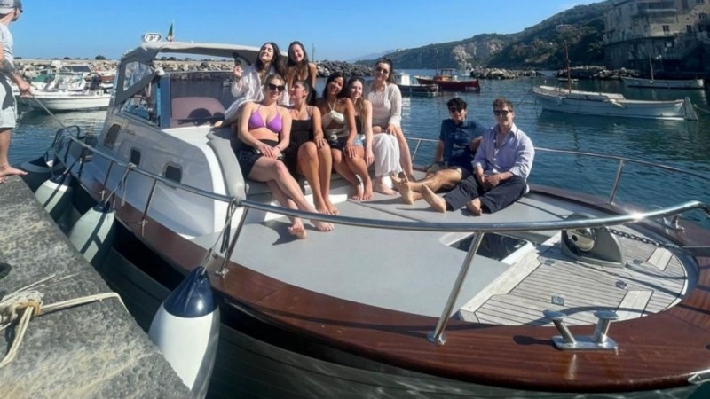Group of people sitting on a boat docked by a waterfront under a clear blue sky.