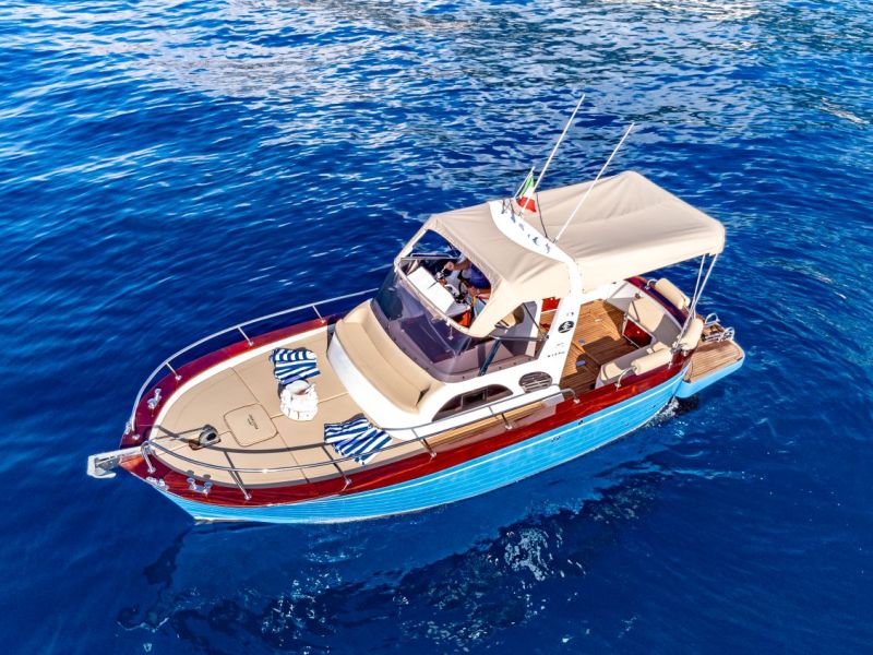 A small yacht with a canopy is floating on clear blue water.